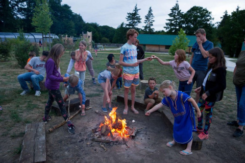 Niños y adultos reunidos alrededor de una fogata en Village Huttopia Senonches, un parque vacacional en Centre-Val de Loire, Francia.