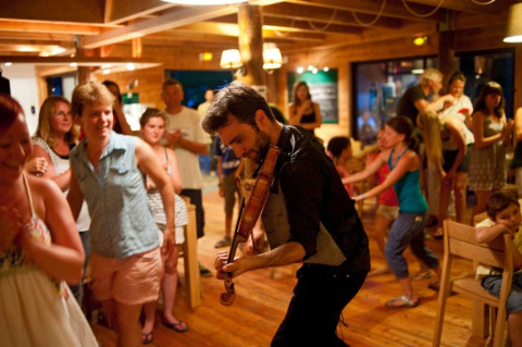 Een violist treedt op voor vrolijke vakantiegangers in een houten chalet bij Village Huttopia Senonches, Frankrijk.