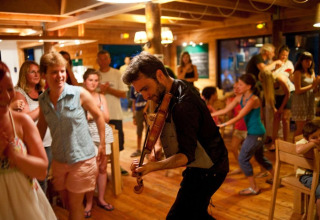 Ein Geiger spielt für fröhliche Urlauber in einer Holzhütte im Village Huttopia Senonches in Frankreich.