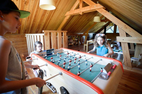 Kinderen spelen tafelvoetbal op een warme houten zolder in Village Huttopia Senonches, Centre-Val de Loire.