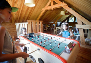 Kinderen spelen tafelvoetbal op een warme houten zolder in Village Huttopia Senonches, Centre-Val de Loire.