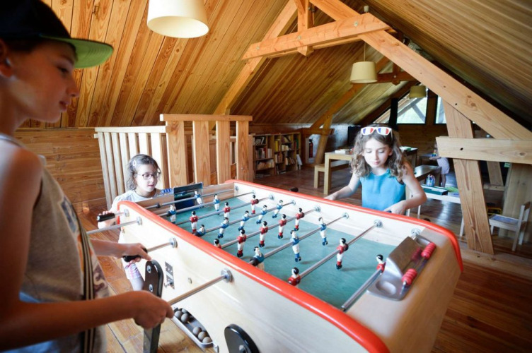 Children playing foosball in a cozy wooden attic at Village Huttopia Senonches holiday park in Centre-Val de Loire.