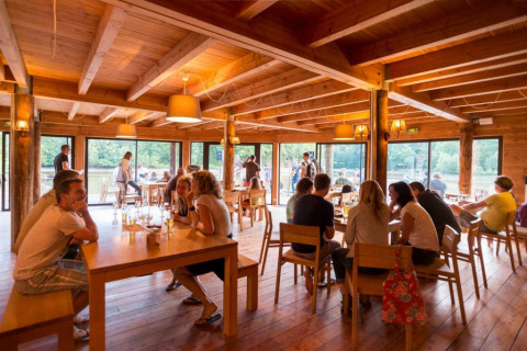 Restaurante de parque vacacional con interior de madera y huéspedes en Village Huttopia Senonches, Centro-Val de Loire, Francia.