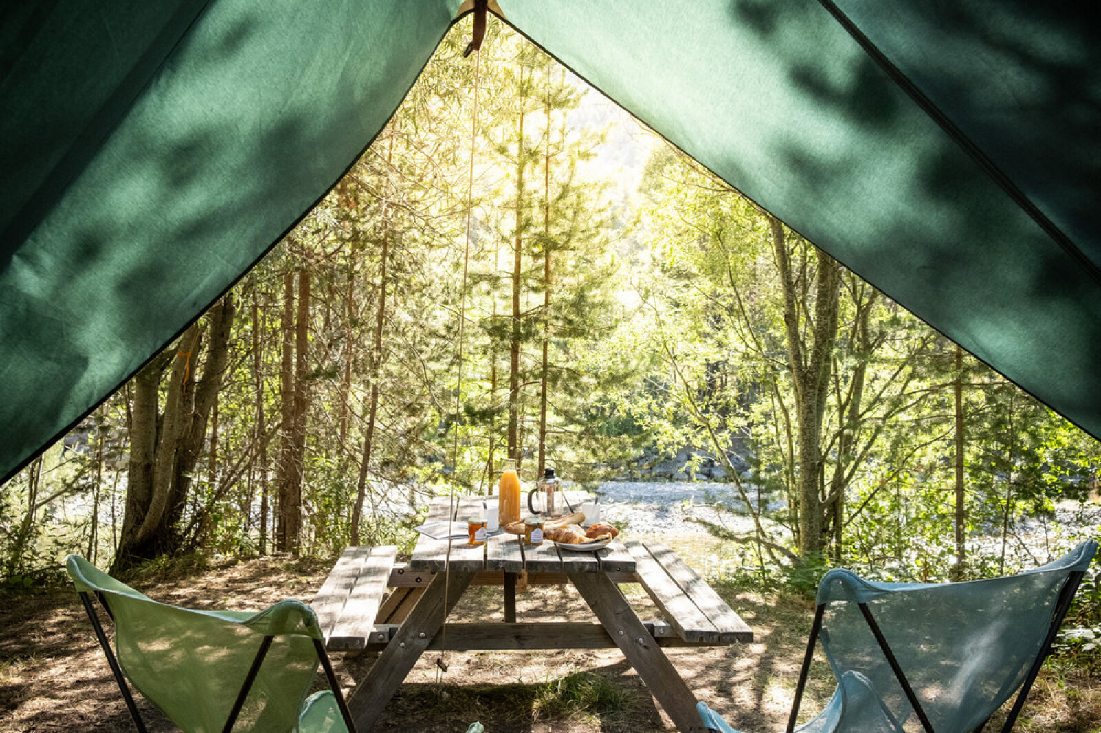 Uitzicht vanuit een tipi tent Bonaventure op een picknicktafel met ontbijt in een zonnig bosgebied.