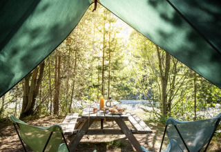 Udsigt fra en tipi telts åbning mod et træ-bord, morgenmad og natur ved Bonaventure campingplads.