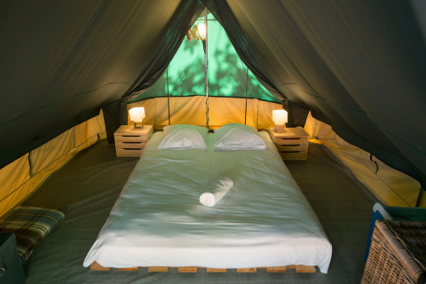 Interiør af Bonaventure teepee telt med en dobbeltseng, to natborde og to lamper under teltdug.