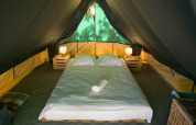 Interieur van Bonaventure tipi tent met tweepersoonsbed, nachtkastjes en lampen onder het tentzeil.