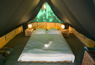 Interiør af Bonaventure teepee telt med en dobbeltseng, to natborde og to lamper under teltdug.