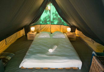 Innenraum des Bonaventure-Tipizelts mit Doppelbett, zwei Nachttischen und Lampen unter Stoffdach.