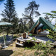 Tienda tipi Bonaventure sobre plataforma de madera en el bosque, con sillas, sombrilla y montañas.