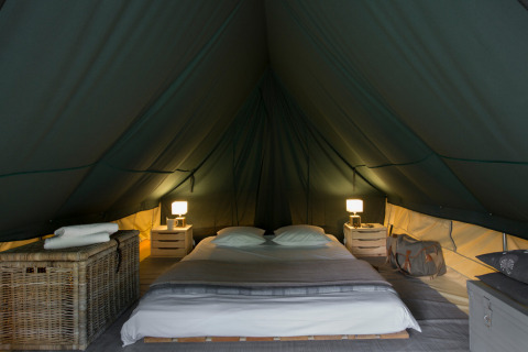 Interior de la tienda tipi Bonaventure con cama doble, mesitas, lámparas y un ambiente acogedor.