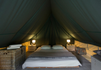 Interno della tenda tipi Bonaventure con letto doppio, comodini, lampade e atmosfera accogliente.