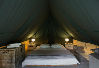Interior of Bonaventure teepee tent with double bed, nightstands, lamps, and a cozy atmosphere.