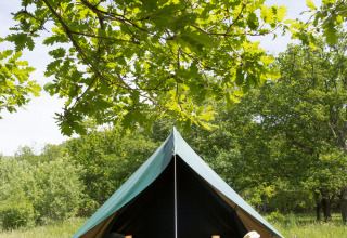 La tienda tipi Bonaventure en Village Huttopia Sud-Ardèche, Francia, rodeada de césped alto y árboles verdes.