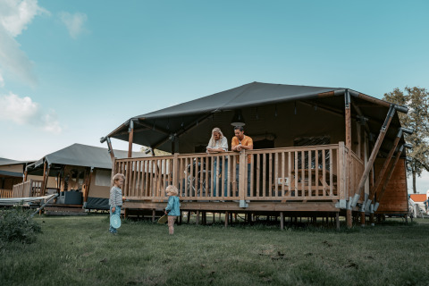Familie genießt den Aufenthalt auf der Veranda einer Holzhütte, während Kinder draußen auf dem Rasen spielen.