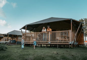 Familia relajándose en la terraza de una cabaña mientras dos niños juegan en el césped frente al lodge.