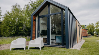 Casa pequeña Oslo Suite moderna con grandes ventanales de vidrio y dos sillas blancas en el césped.