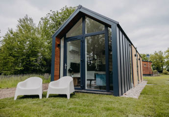 Moderne Oslo Suite tiny house med store glasvinduer, grøn græsplæne og to hvide stole udenfor.