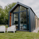 Moderne Oslo Suite tiny house med store glasvinduer, grøn græsplæne og to hvide stole udenfor.