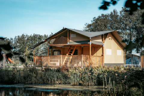 Vista esterna della Ranger Lodge, immersa nel verde, con veranda in legno e stagno di fronte.