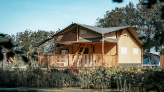 Vista exterior de la Ranger Lodge, rodeada de vegetación, con terraza de madera y un estanque adelante.