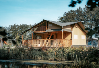 Vista esterna della Ranger Lodge, immersa nel verde, con veranda in legno e stagno di fronte.