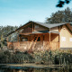 Vista exterior de la Ranger Lodge, rodeada de vegetación, con terraza de madera y un estanque adelante.