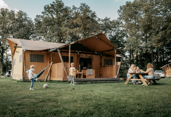 Familia disfruta del aire libre en una gran tienda Safari Lodge, niños juegan en el césped frente a la tienda.