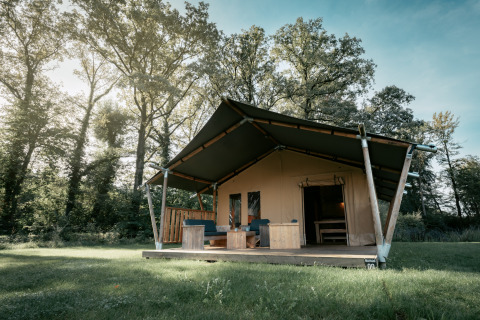Une grande tente safari appelée Nomad XL installée sur une prairie et entourée d'arbres imposants.