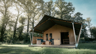 Una amplia tienda safari llamada Nomad XL situada en un claro de césped rodeado de árboles.