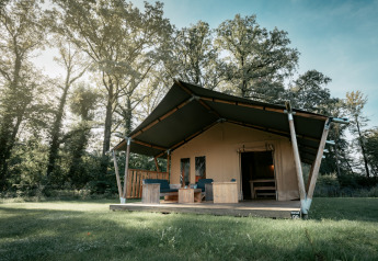 Una amplia tienda safari llamada Nomad XL situada en un claro de césped rodeado de árboles.