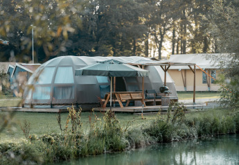 Panorama lodge met moderne koepeltent, terras met parasol en uitzicht op het meer en het bos.