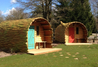 Dos acogedoras cabañas con forma de tronco de árbol y puertas de colores rodeadas de naturaleza y césped.