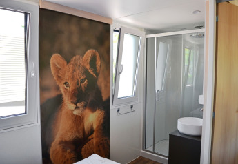 Interior view of SunLodge Sabai at Camping Gasparina in Italy, featuring a lion cub mural and bathroom.