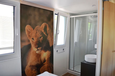 Vue intérieure de la SunLodge Sabai au Camping Gasparina, avec une fresque de lionceau et salle de bains.