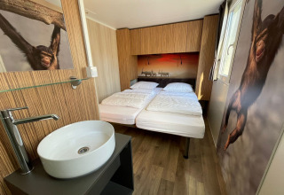 Habitación moderna con cama doble, arte de animales y lavabo en SunLodge Sabai, Camping Gasparina, Italia.