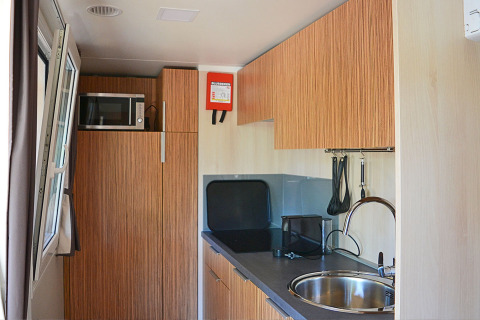 Coin cuisine de la SunLodge Sabai au Camping Gasparina en Italie, avec micro-ondes, évier et placards bois.