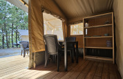 Vista interior de una tienda safari en Camping Luna del Monte en Italia con mesa y estantería.
