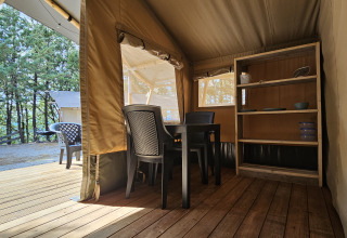 Vista interior de una tienda safari en Camping Luna del Monte en Italia con mesa y estantería.