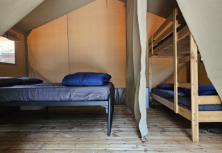 Interior de una tienda safari en Camping Luna del Monte, Italia, con una cama doble y literas visibles.