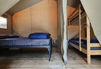 Interior de una tienda safari en Camping Luna del Monte, Italia, con una cama doble y literas visibles.