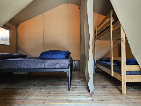 Interno di una tenda safari al Camping Luna del Monte in Italia con letto matrimoniale e letto a castello.