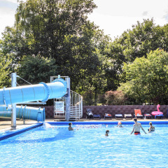 Piscina exterior con gran tobogán azul y visitantes en Veluwecamping 't Schinkel, en Gelderland, Países Bajos.