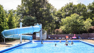 Piscina exterior con gran tobogán azul y visitantes en Veluwecamping 't Schinkel, en Gelderland, Países Bajos.