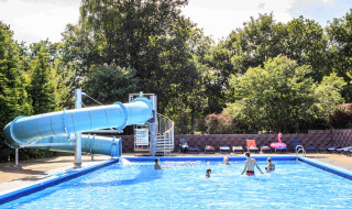 Piscina exterior con gran tobogán azul y visitantes en Veluwecamping 't Schinkel, en Gelderland, Países Bajos.