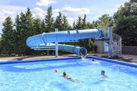 Piscina exterior con gran tobogán azul en Veluwecamping 't Schinkel, niños disfrutando del agua y el sol.