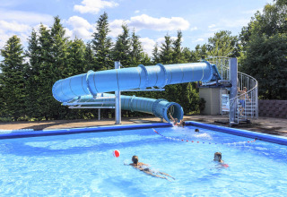 Piscina exterior con gran tobogán azul en Veluwecamping 't Schinkel, niños disfrutando del agua y el sol.