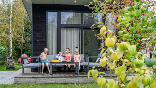 Niños sentados en la terraza de una cabaña River Cabin en Holiday Park Mölke, rodeados de vegetación.