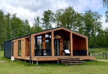 Moderne strandhytte ved Wilsumer Berge i Tyskland omgivet af græsplæner og grønne træer.