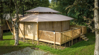 Tienda safari Stardust 40 Family Lodge con terraza de madera en un camping verde y arbolado en verano.